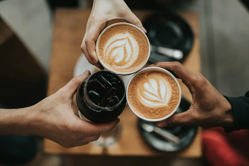 Dos manos sostienen tazas de café con arte latte